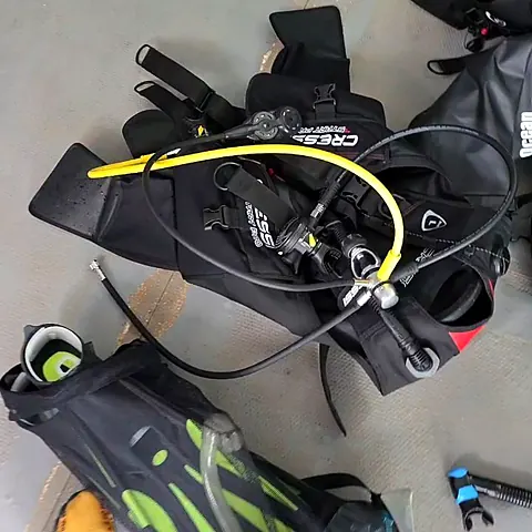 Equipo de buceo en el piso: chaleco, regulador con manguera amarilla, aletas y snorkel