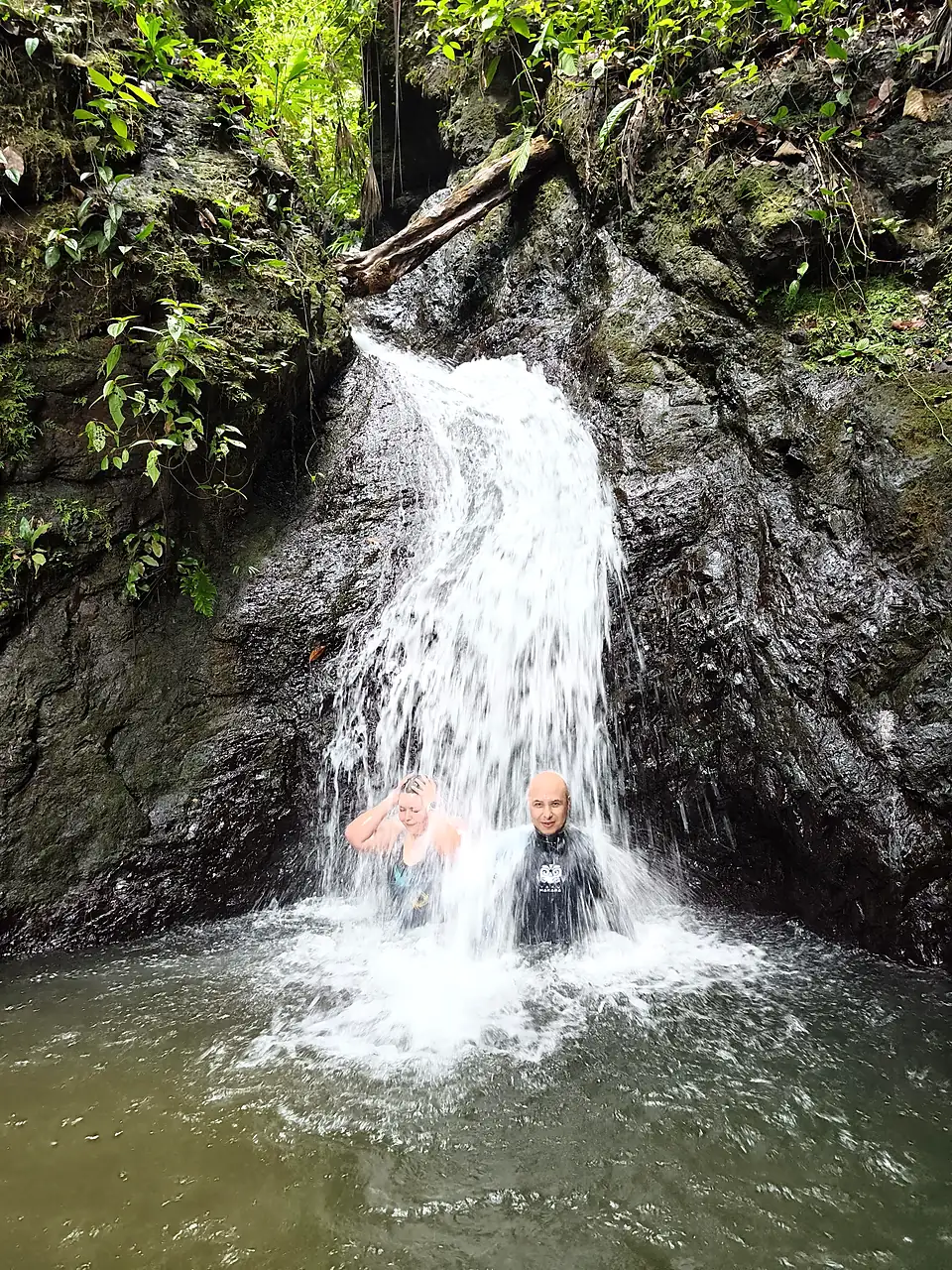 Dos personas bajo una cascada que cae sobre roca negra en plena selva del Pacífico